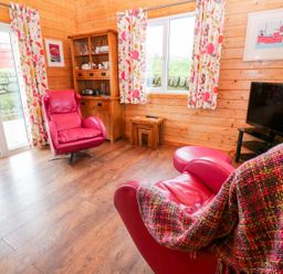 A living room with red leather chairs a wooden cabinet colorful curtains and a TV at Borah Lodge Mousehole