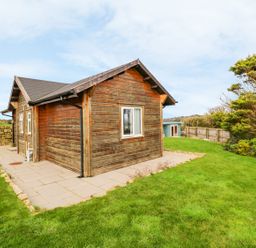 A wooden cabin with a tiled patio and grassy yard at Borah Lodge in Mousehole