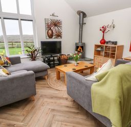A living room with grey sofas a wooden coffee table and a fireplace at Meadowside in Mousehole