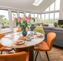 A dining area with a round table and leather chairs next to a living room with gray sofas and a television at Meadowside in Mousehole