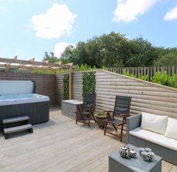 An outdoor deck with a hot tub chairs and sofa with cushions at Willow Retallack in Retallack near St Columb Major