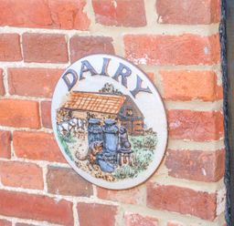A brick wall with a round ceramic plaque showing a dairy scene at The Dairy Barn in Toftrees near Fakenham