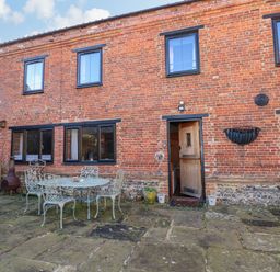 A brick building with multiple windows and doors a patio area with metal table and chairs at The Dairy Barn in Toftrees near Fakenham