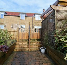 A backyard garden with wooden fencing plants and stone steps leading to a two story stone house at Tawny Cottage in Irton Moor near Scarborough