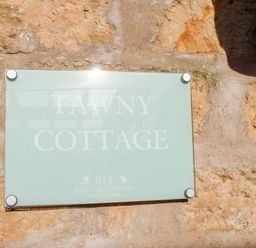 A glass sign on a stone wall with text Tawny Cottage at Riggs Head Farm country cottages