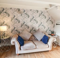 A beige sofa with cushions between two round metal side tables with a lamp and small chalkboard under slanted ceiling at Tawny Cottage Irton Moor near Scarborough
