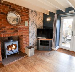 A living room with a wood-burning stove in a brick fireplace and a television on a stand near glass doors at Tawny Cottage in Irton Moor near Scarborough