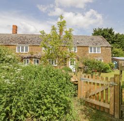 A garden with plants and a wooden gate in front of a stone house at Priors Mead in Claydon near Cropredy
