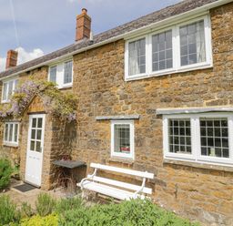 Stone cottage exterior with white door bench and flowering plants at Priors Mead Claydon near Cropredy