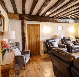 A living room with leather sofas armchair wooden beams and a door at Cwm Yr Afon Mawr in Llanbedr near Harlech