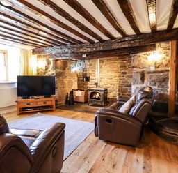 A living room with leather armchairs a wood burning stove stone walls television and wooden ceiling beams at Cwm Yr Afon Mawr in Llanbedr near Harlech