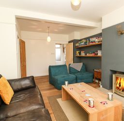 A living room with a brown leather sofa two blue chairs a wooden coffee table with mugs and cards a fireplace and shelves with board games at Sandsfoot Rest in Weymouth