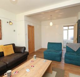 A living room with a brown leather sofa two blue chairs a wooden coffee table and shelves with board games at Sandsfoot Rest in Weymouth