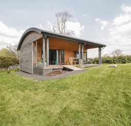 A small wooden cabin with a curved roof and porch on a grassy lawn at Foxglove in Sticklinch West Pennard Glastonbury