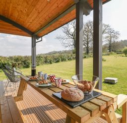 A wooden picnic table with bread and croissants on a covered patio overlooking a grassy field at Foxglove in Sticklinch West Pennard Glastonbury