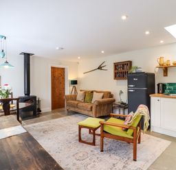 A living room with a sofa an armchair a wood stove a dining table and an open kitchen at Courtyard Cottage Poplar Farm Barn in Sweffling near Saxmundham