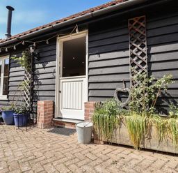 The exterior of a building with a white half door black wooden siding several potted plants and a brick paved patio at Courtyard Cottage Poplar Farm Barn Sweffling near Saxmundham