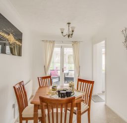 A dining room with wooden table and chairs and glass doors leading to a sitting area at Casa Carmen in Weymouth