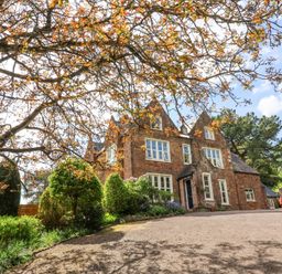 A stone house with multiple windows and a driveway surrounded by trees and shrubs at The Old Vicarage in Tiverton
