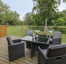 An outdoor deck with a glass table and four chairs overlooking a grassy area and a pond at The Barn in Droitwich Spa