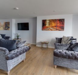 A living room with two grey sofas a wall-mounted TV autumn landscape paintings and a small table with flowers at Low Tide in Weymouth