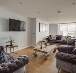 A living room with three dark sofas a wooden coffee table and a wall-mounted TV at Low Tide in Weymouth
