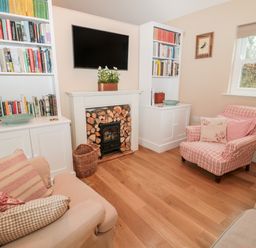 A living room with built in bookshelves a television above a fireplace and upholstered armchairs at The Garden Cottage in West Woodburn