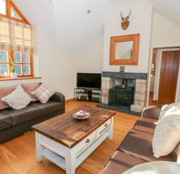 A living room with two brown sofas a wooden coffee table a fireplace and a television at Bwthyn Carregwen in Dwygyfylchi