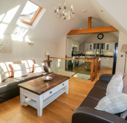 A living room with two brown sofas a wooden coffee table and a kitchen in the background at Bwthyn Carregwen in Dwygyfylchi