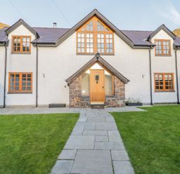 A house with multiple windows and a central wooden door with a stone pathway and a green lawn at Bwthyn Carregwen in Dwygyfylchi