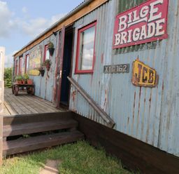 An exterior view of a weathered metal-sided cabin with wooden steps and potted plants at Crows Cabin in Gloucester