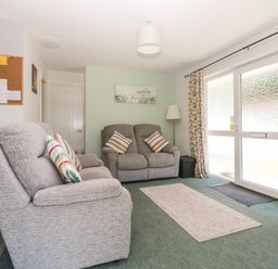 A living room with two grey sofas and striped cushions near large frosted glass doors at Tranquillity Rosecraddoc Lodge near Liskeard