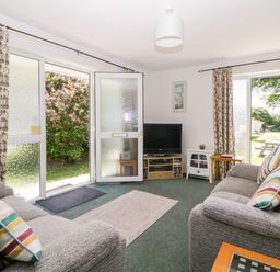 A living room with two sofas a television and open doors to the garden at Tranquillity Rosecraddoc Lodge near Liskeard
