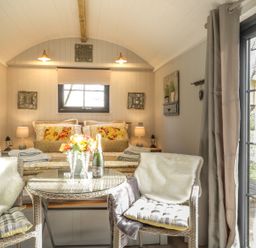 A bedroom with a bed pillows and lamps with two chairs and a table with flowers and champagne in High Rigg Shepherds Delight in Brampton Cumbria