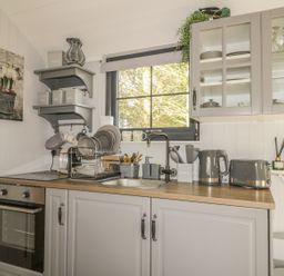 A kitchen with grey cabinets a countertop with appliances and dish rack under a window at High Rigg Shepherd's Delight in Brampton Cumbria