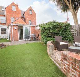 A backyard garden with artificial grass a patio table with chairs and a seating area with wicker chairs and a glass table at Brewers House in Weymouth