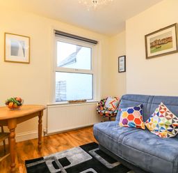 A small living room with a wooden table and chairs a window a blue sofa with colorful cushions a patterned chair and pictures on the walls at Brewers House in Weymouth