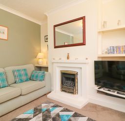 A living room with a sofa with patterned cushions a fireplace a wall mirror a television on a shelf and a collection of DVDs on built-in shelves at Brewers House in Weymouth