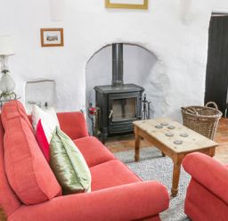 A living room with red sofas a wooden coffee table a black wood stove and a wicker basket at An Teach Ban in Rossaveel County Galway