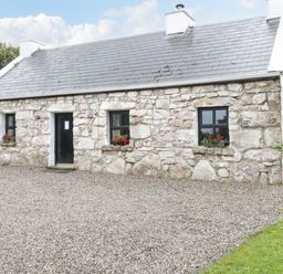 A stone cottage with three black windows and a black door surrounded by gravel at An Teach Ban in Rossaveel County Galway