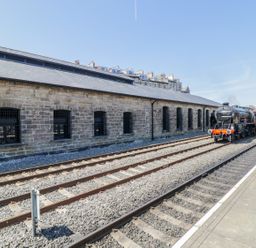 A railway station platform with tracks a stone building and a steam locomotive at Evening Star @ Engine Shed in Whitby