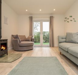 A living room with a wood stove a round armchair a sofa and glass doors with curtains at Kober House in Mullion
