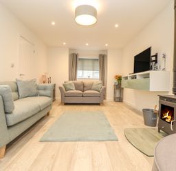 A living room with sofas a rug a wood burning stove and a wall mounted television at Kober House in Mullion