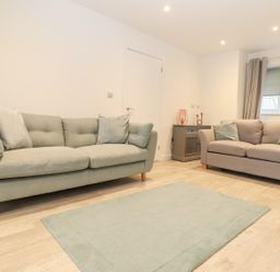 A living room with two sofas a small cabinet with decorations and a rug on the floor at Kober House in Mullion