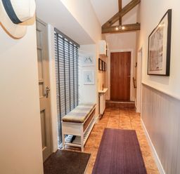 A hallway with a cushioned bench near window blinds and a wooden door at Hemmel Cottage in Chatton