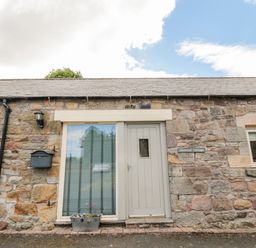 Stone exterior wall with a door and window with flowerpot and mailbox at Hemmel Cottage in Chatton