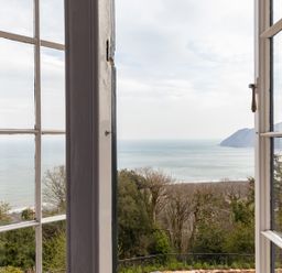 A view of the sea and hills through open glass windows at Bayview Terrace in Lynton