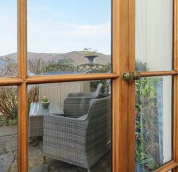 Wood framed glass doors opening to a patio with wicker chairs and a table with plants at Bayview Terrace in Lynton