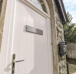 A white door with a metal handle and a sign that reads Capel Horeb stone wall and a mailbox outside at Horeb Chapel House in Tanygrisiau