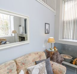 A living room with a patterned sofa and cushions a lamp on a tree stump table firewood in a basket and a window with blinds at Horeb Chapel House in Tanygrisiau